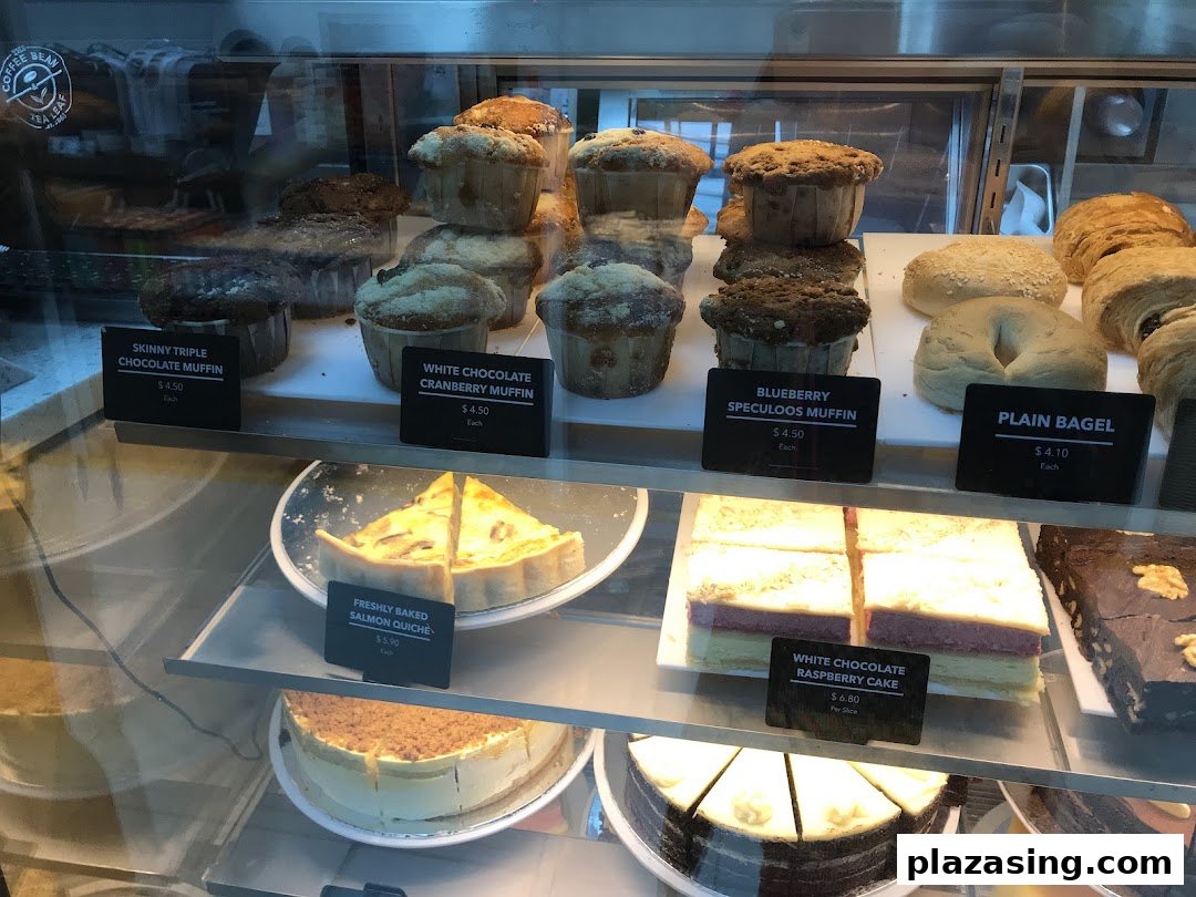 A display case showcasing a variety of freshly baked muffins, bagels, quiche, and cakes.