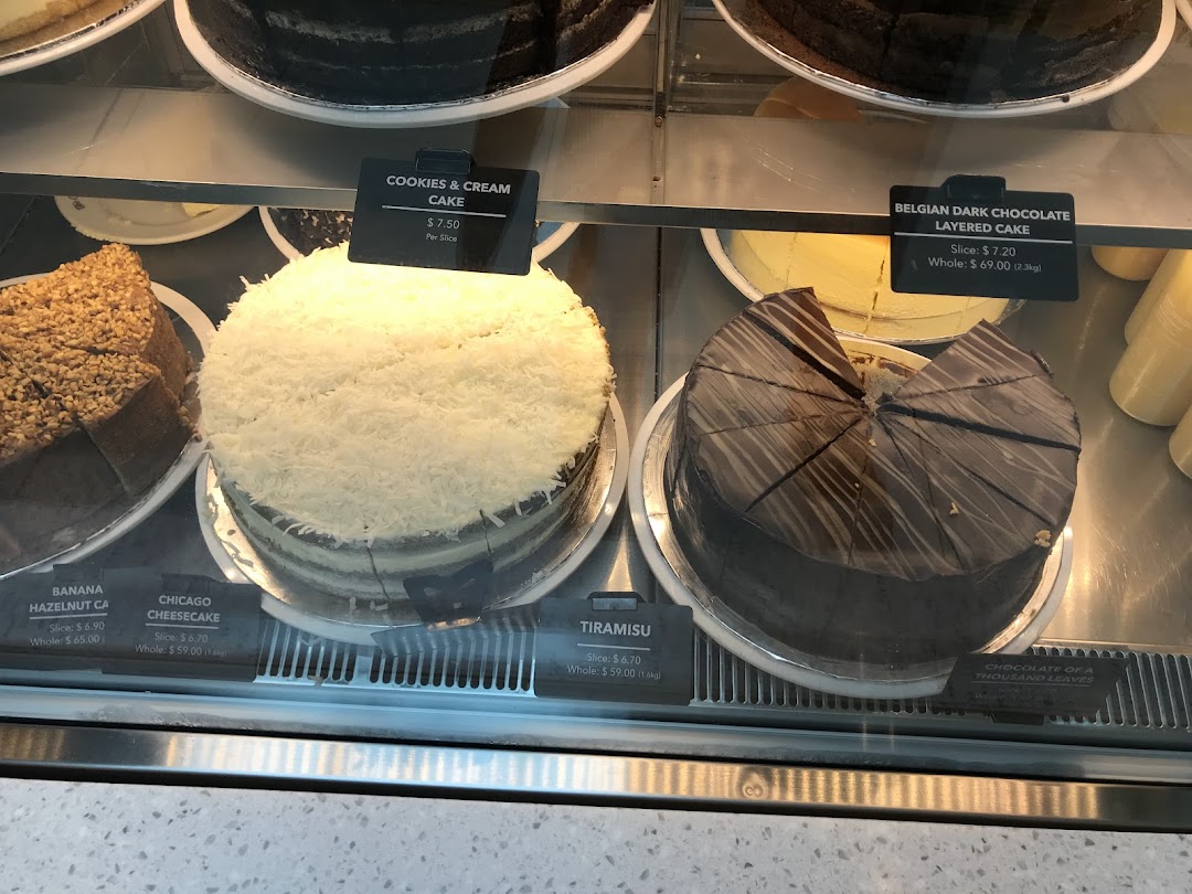 A display case showcasing various whole and sliced cakes with their names and prices.