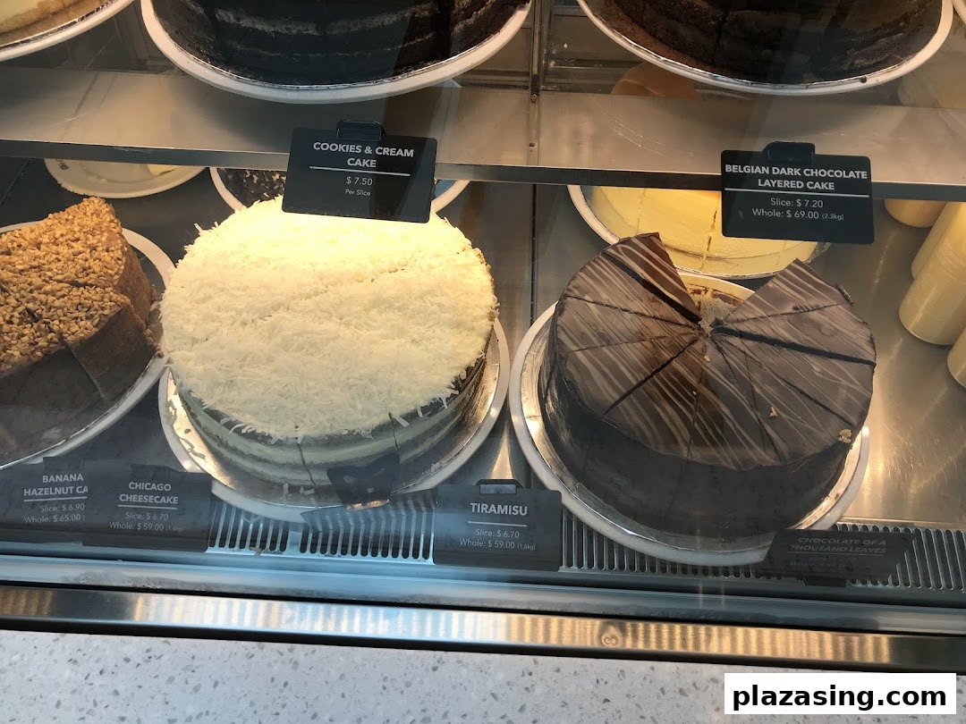 A display case showcasing various whole and sliced cakes with their names and prices.