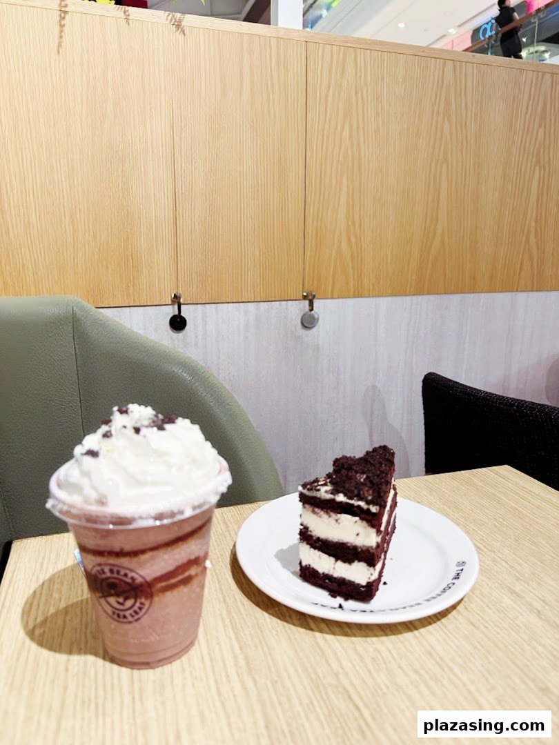 A red velvet cake slice and a chocolate frappe with whipped cream on a wooden table.