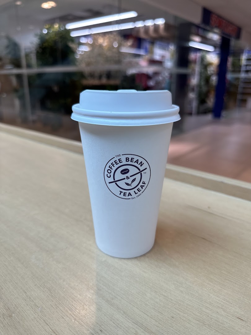 A white coffee cup from The Coffee Bean & Tea Leaf on a wooden surface.