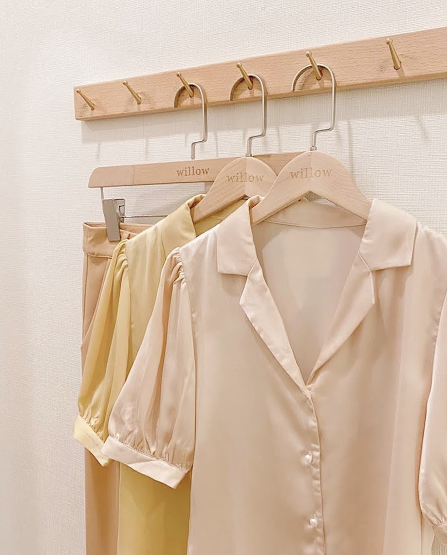 Elegant blouses in soft hues displayed on wooden hangers at The Willow Label.