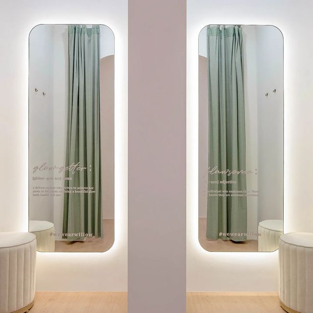 Illuminated mirrors in a stylish fitting room with light green curtains and white stools at The Willow Label.