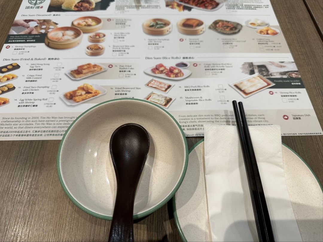 A close-up of Tim Ho Wan's dim sum menu, showing various dishes, prices, and a table setting.