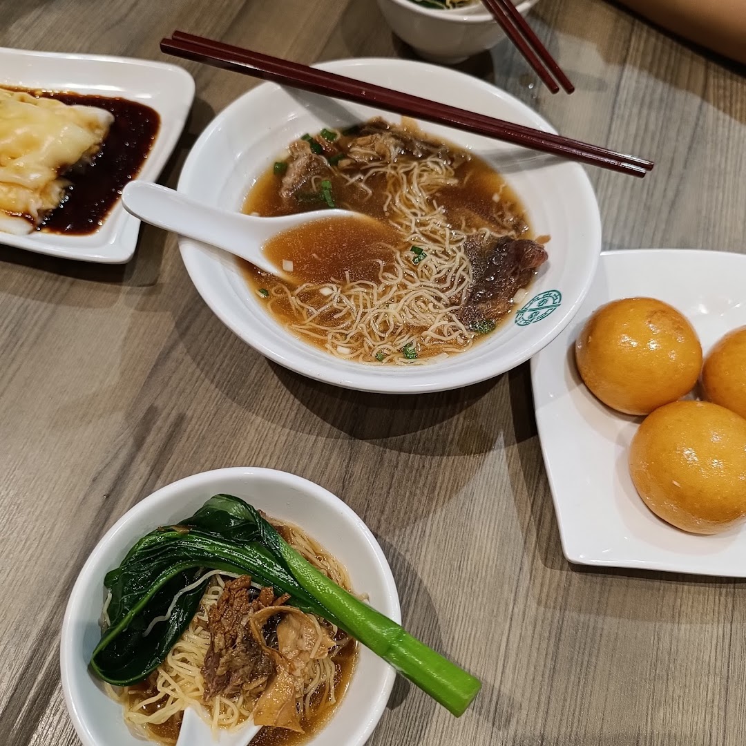 A table laden with delicious Tim Ho Wan dishes, including noodles, rice rolls, and golden fried buns.