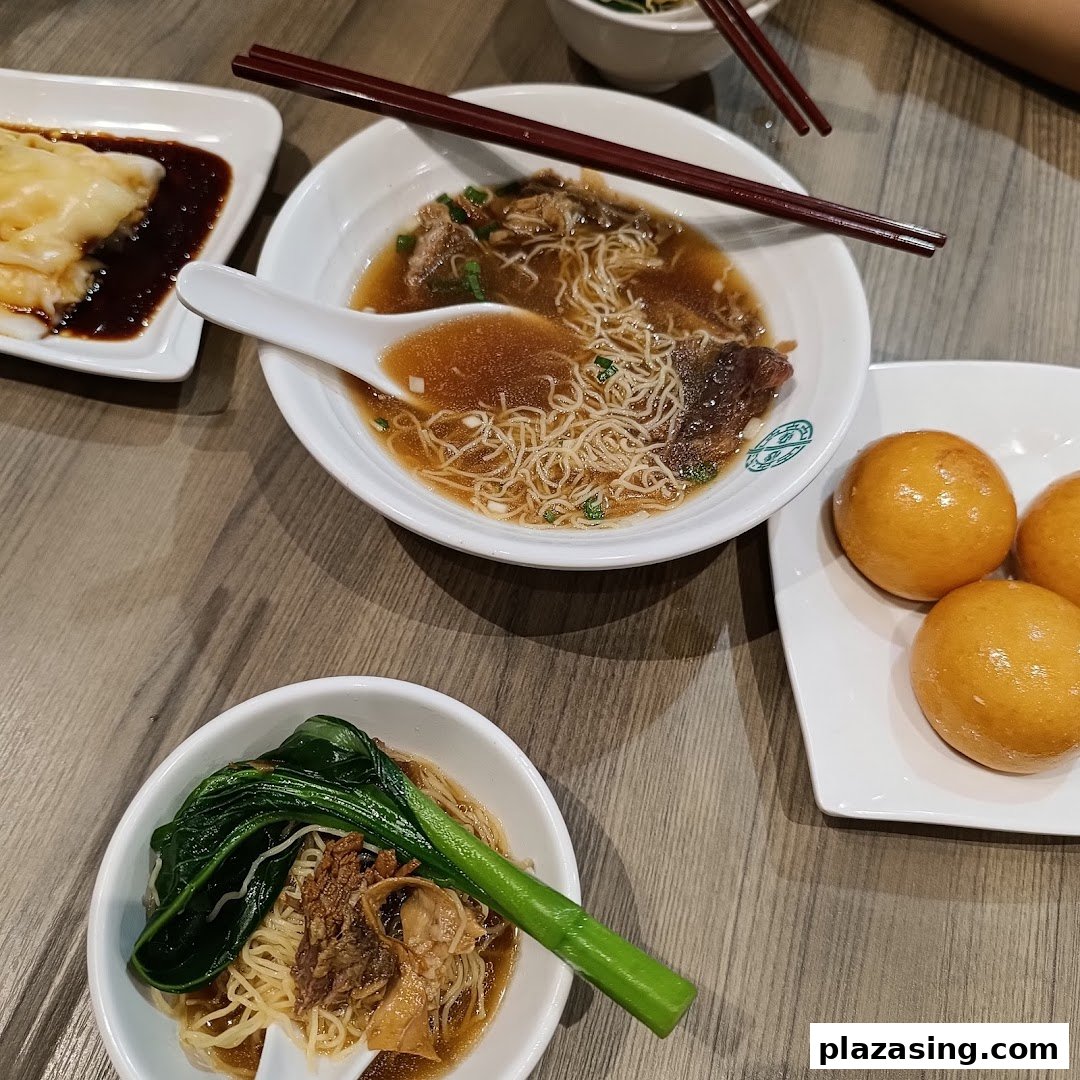 A table laden with delicious Tim Ho Wan dishes, including noodles, rice rolls, and golden fried buns.