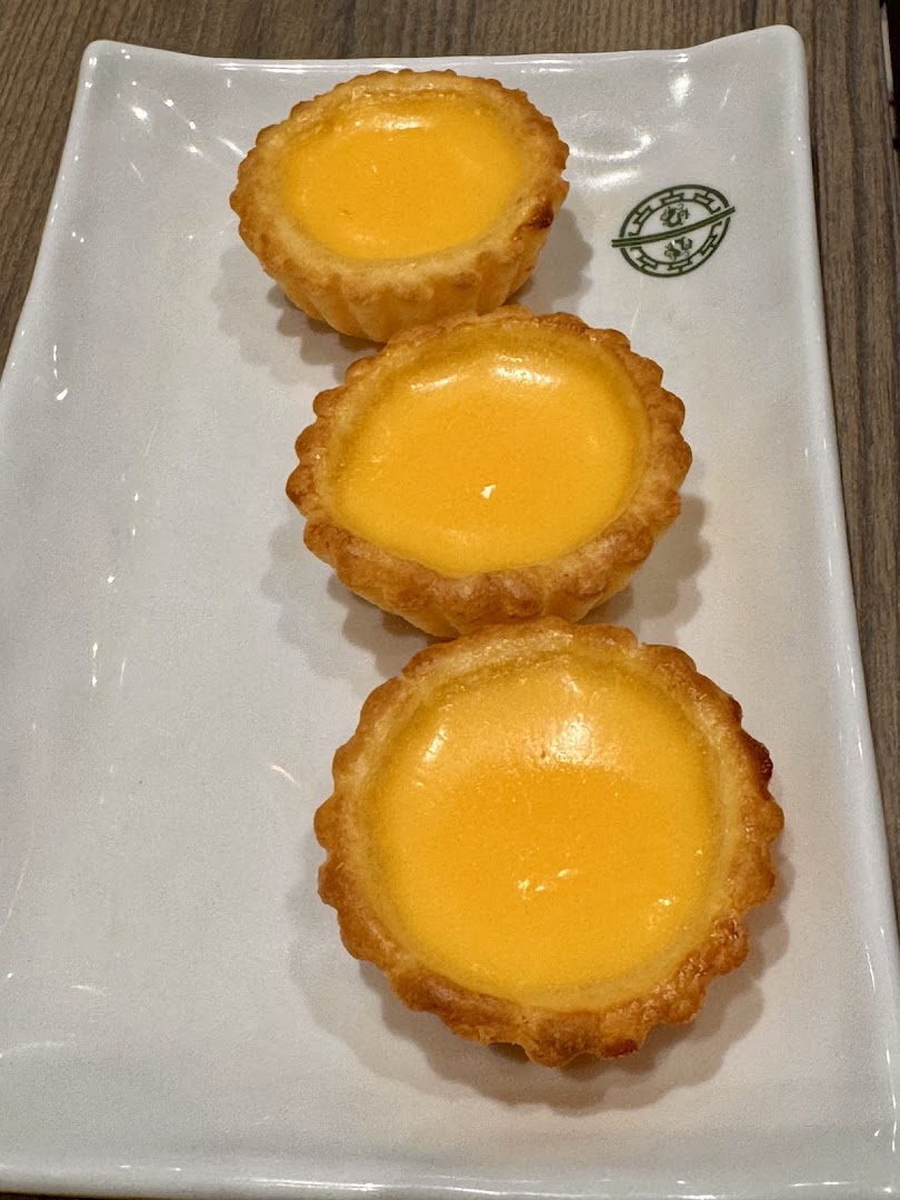 Three golden egg tarts are neatly arranged on a white rectangular plate, showcasing their delicious appearance.