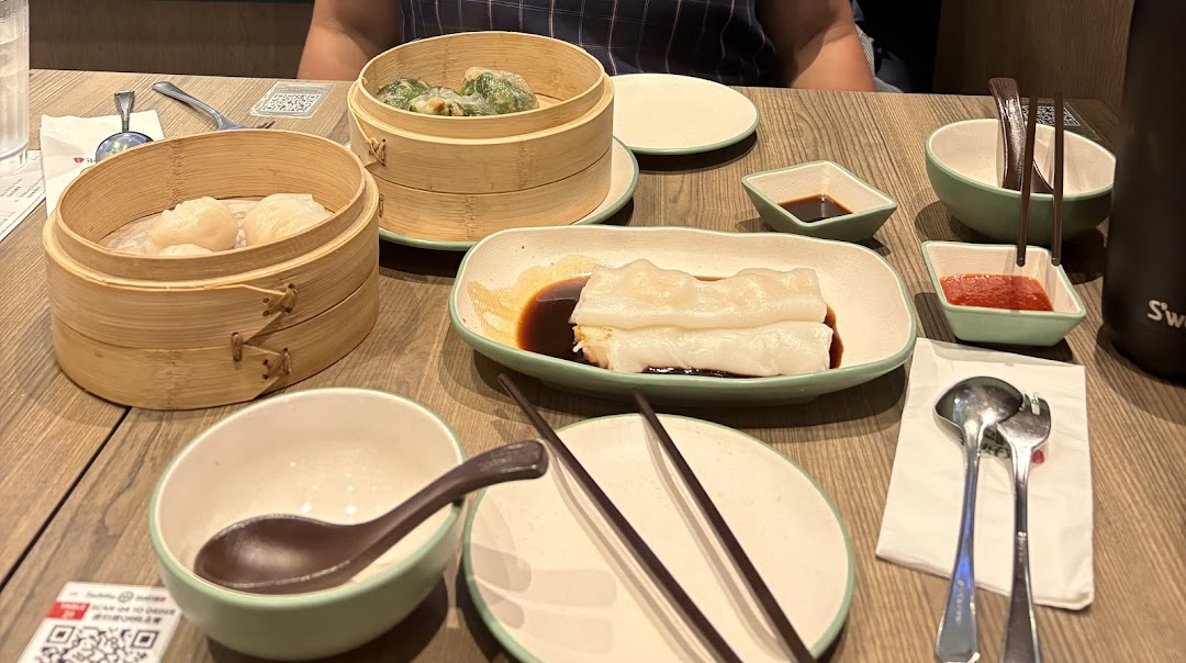 A table laden with various dim sum dishes, including steamed dumplings and rice rolls, at Tim Ho Wan.