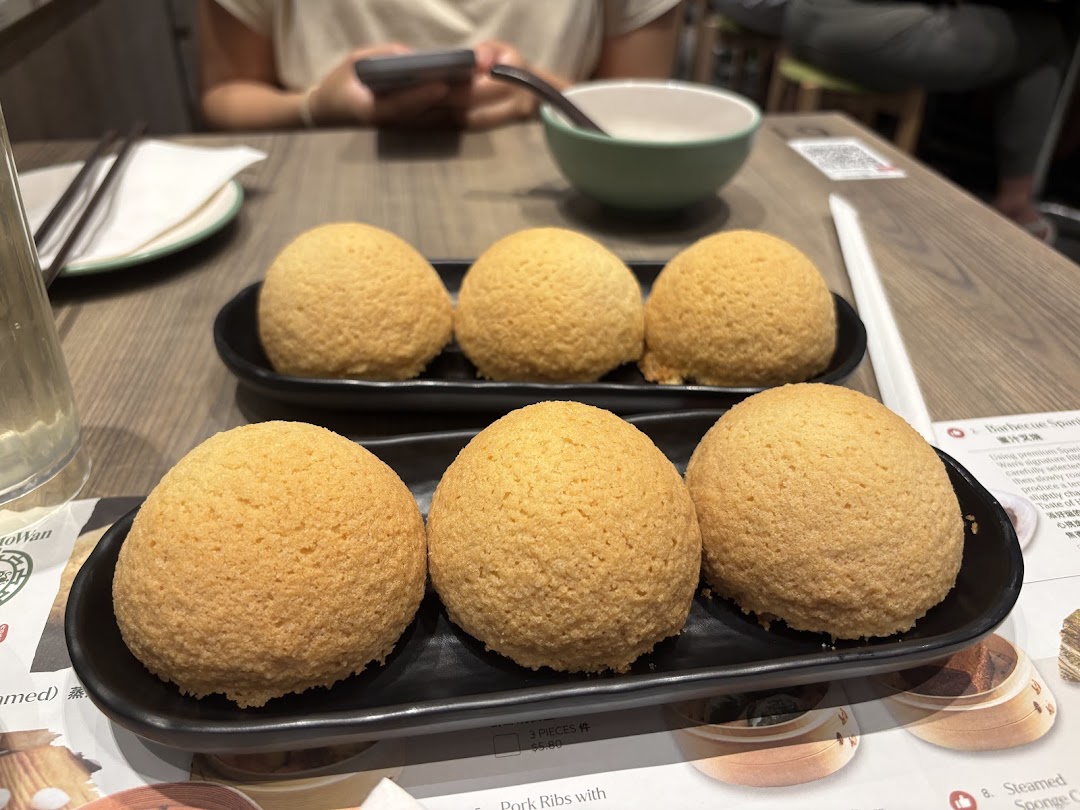 A close-up of six golden-baked buns, likely Tim Ho Wan's famous BBQ pork buns, on black plates.
