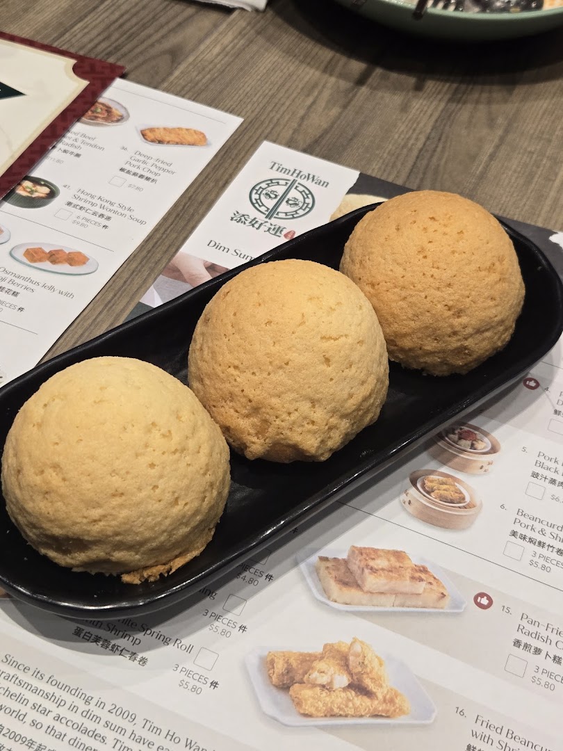 Three signature baked buns on a plate with a Tim Ho Wan menu in the background.