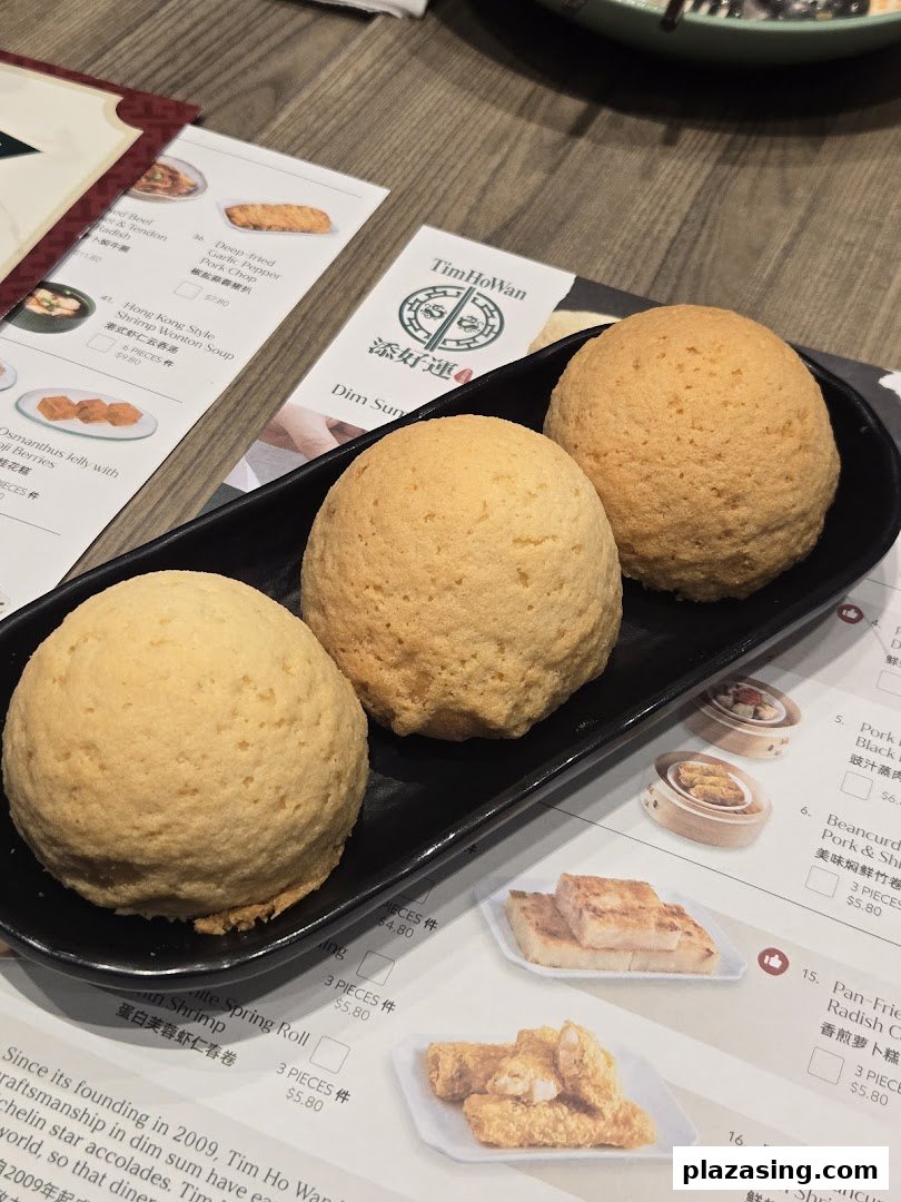Three signature baked buns on a plate with a Tim Ho Wan menu in the background.