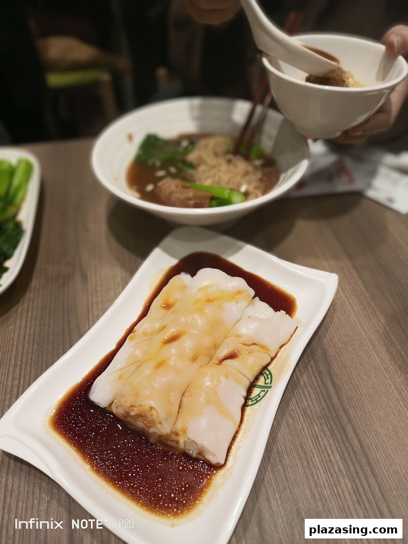 Delicious rice rolls with sauce in the foreground, with a bowl of noodles and vegetables in the background.