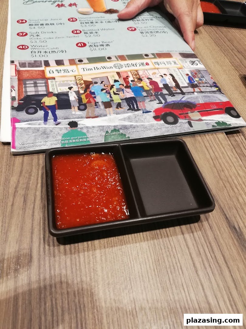 A Tim Ho Wan menu displaying beverages and prices, with a sauce dish on a wooden table.