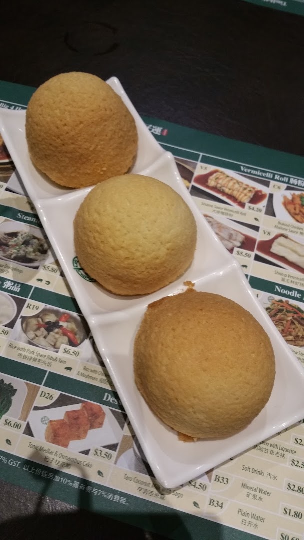 Three golden-brown baked buns on a white plate, with a partial menu displaying various dim sum and drinks.