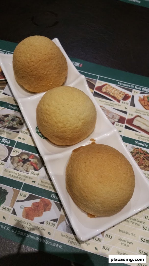 Three golden-brown baked buns on a white plate, with a partial menu displaying various dim sum and drinks.