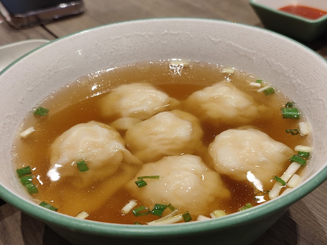 A close-up of a bowl of delicious dumplings in clear broth, garnished with chopped green onions.