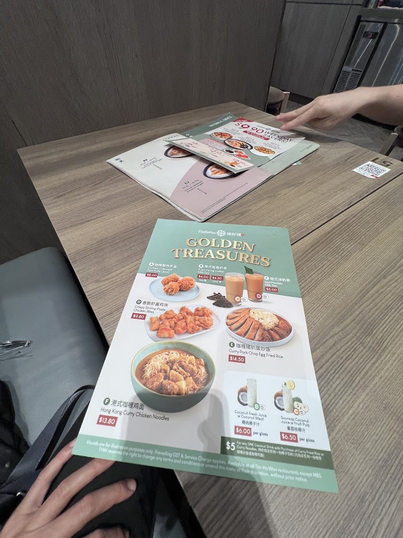 A close-up of a Tim Ho Wan menu displaying various dishes and drinks on a wooden table.