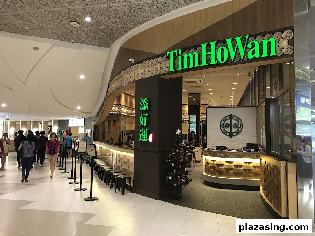 The vibrant green Tim Ho Wan shopfront welcomes diners in a bustling mall setting, featuring a festive Christmas tree.