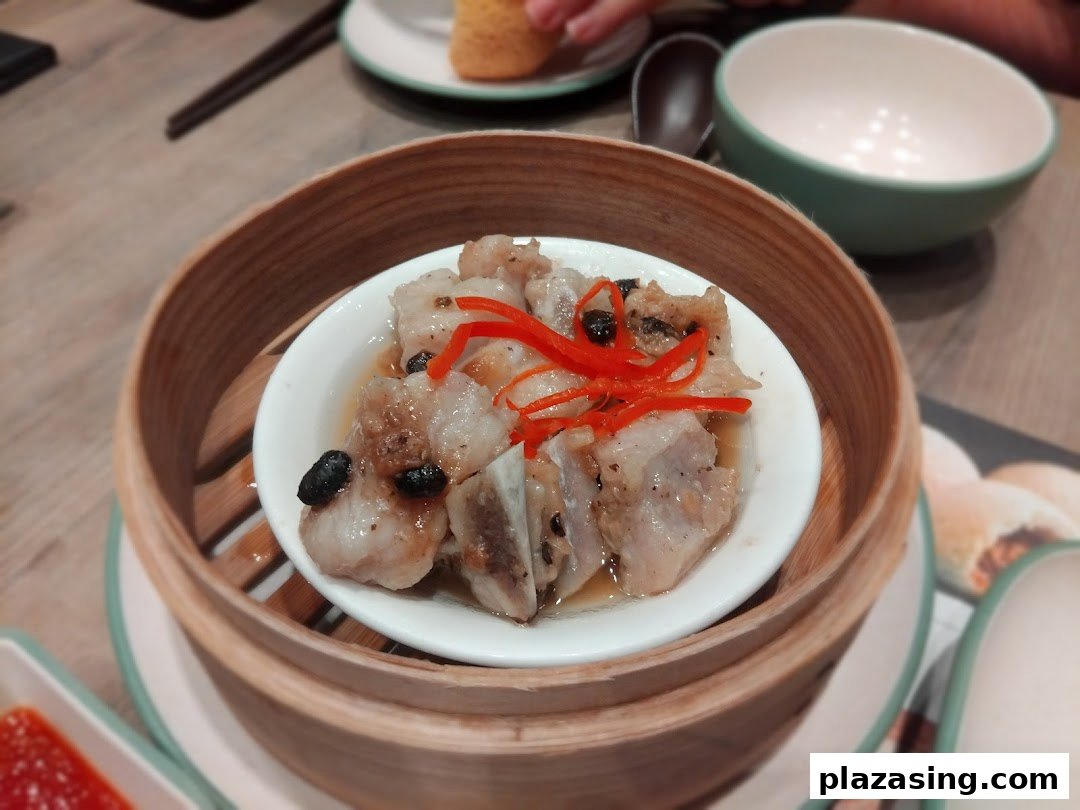A close-up of steamed pork ribs with black beans and chili, served in a traditional bamboo steamer.
