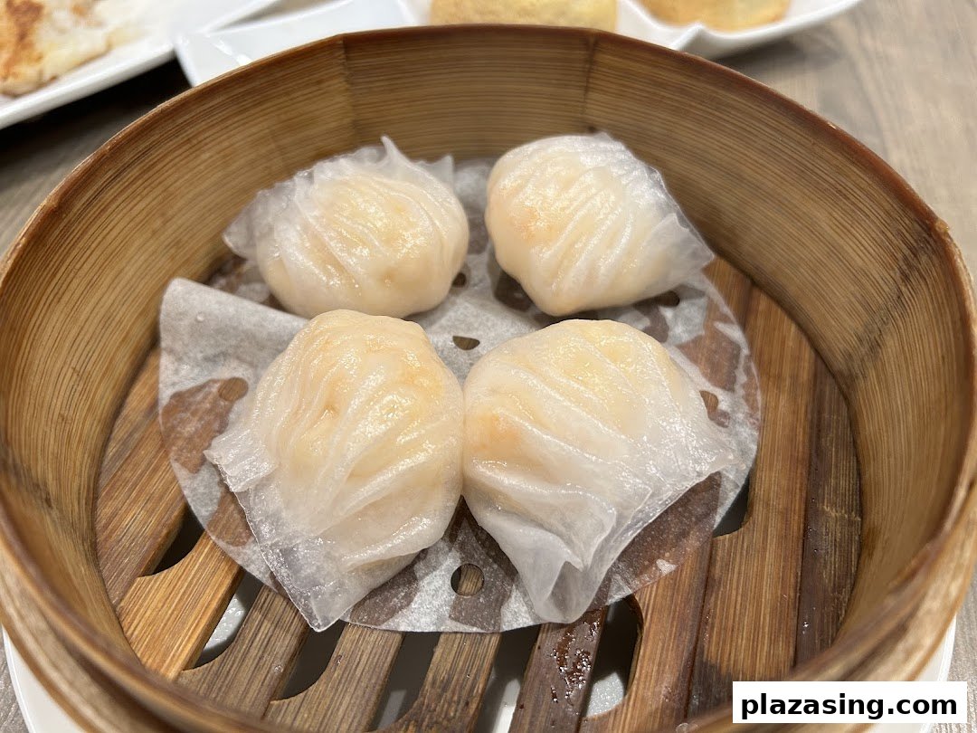 Four perfectly steamed shrimp dumplings (har gow) presented in a traditional bamboo steamer.
