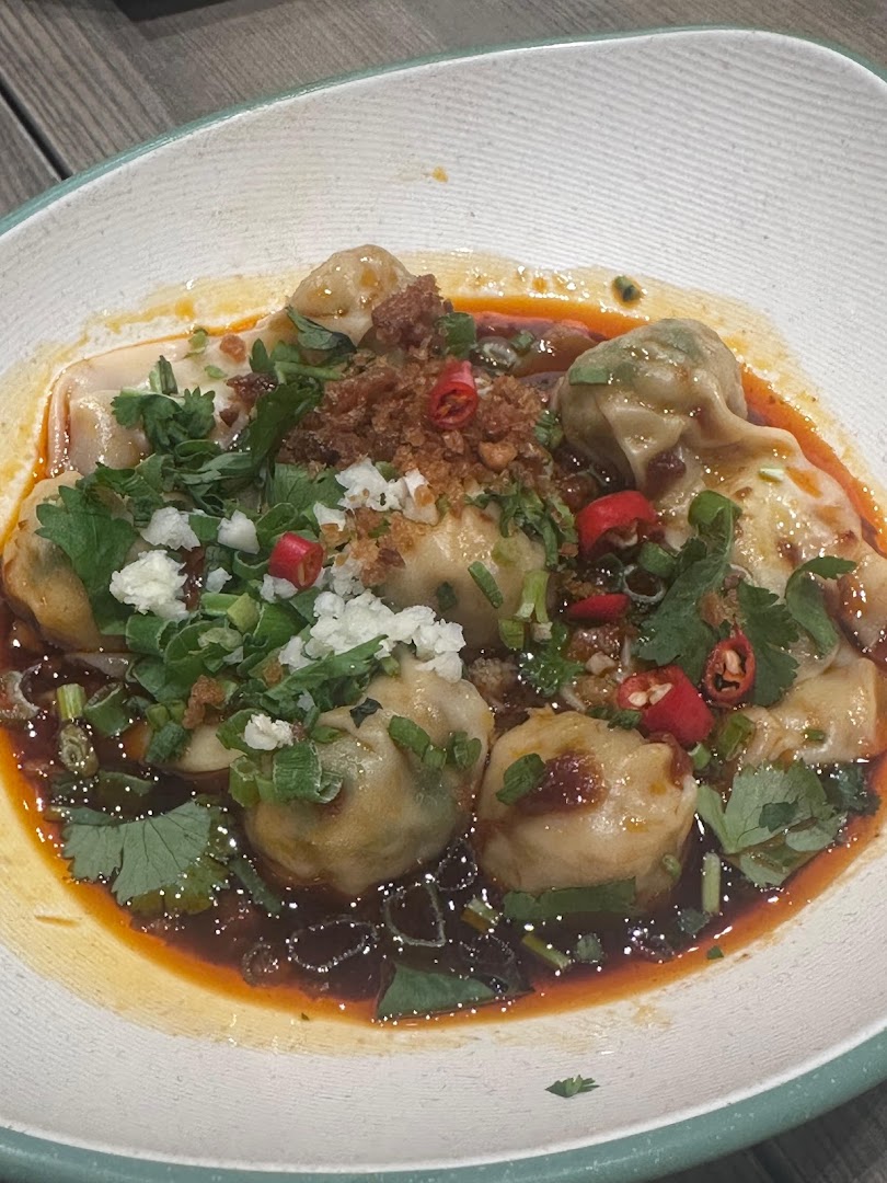 A close-up of delicious dumplings in a spicy sauce, garnished with fresh herbs and chili.