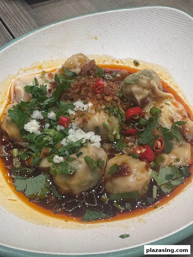 A close-up of delicious dumplings in a spicy sauce, garnished with fresh herbs and chili.