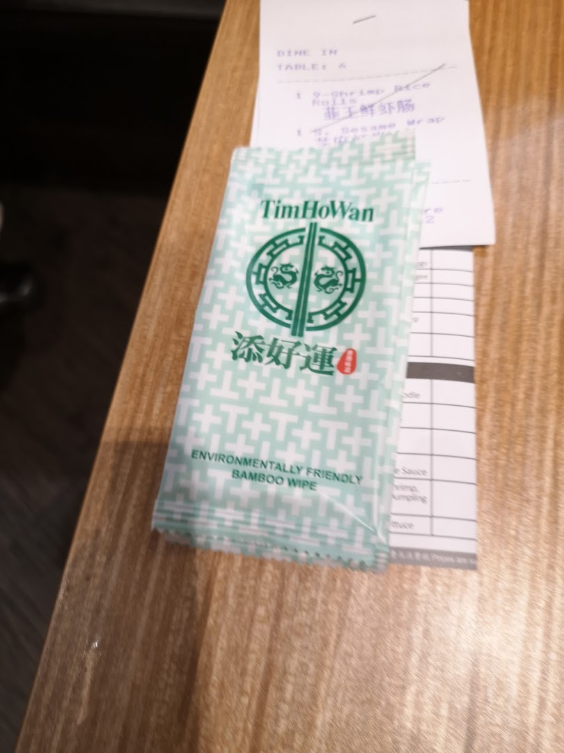 A Tim Ho Wan branded environmentally friendly bamboo wipe and a partial dining receipt on a wooden table.