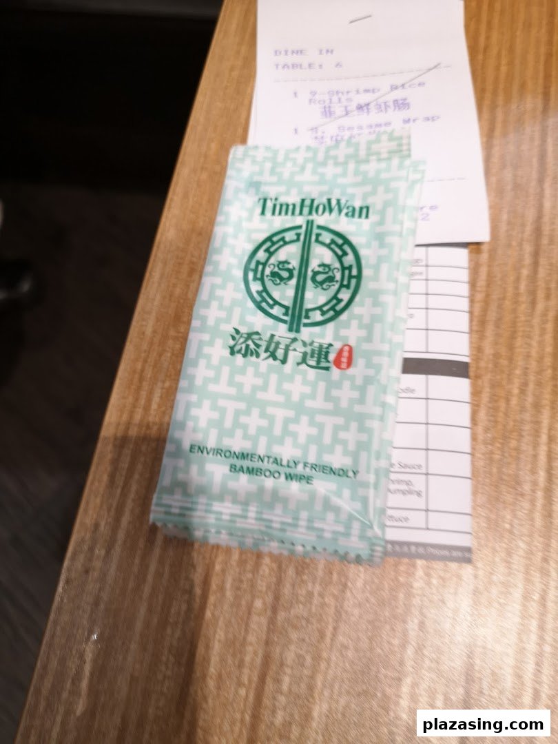A Tim Ho Wan branded environmentally friendly bamboo wipe and a partial dining receipt on a wooden table.