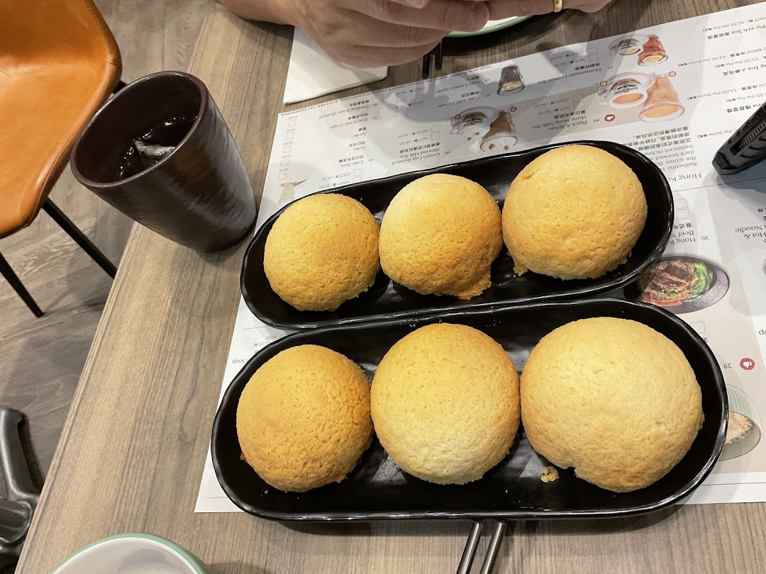 Six golden-baked buns served on black plates with a drink and menu on a wooden table.
