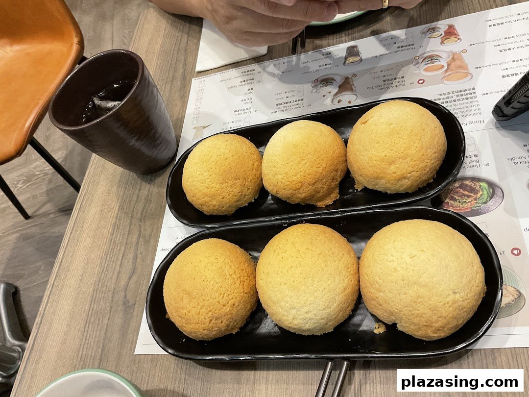 Six golden-baked buns served on black plates with a drink and menu on a wooden table.