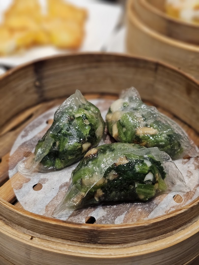 Three vibrant green vegetable dumplings steamed to perfection in a traditional bamboo basket.