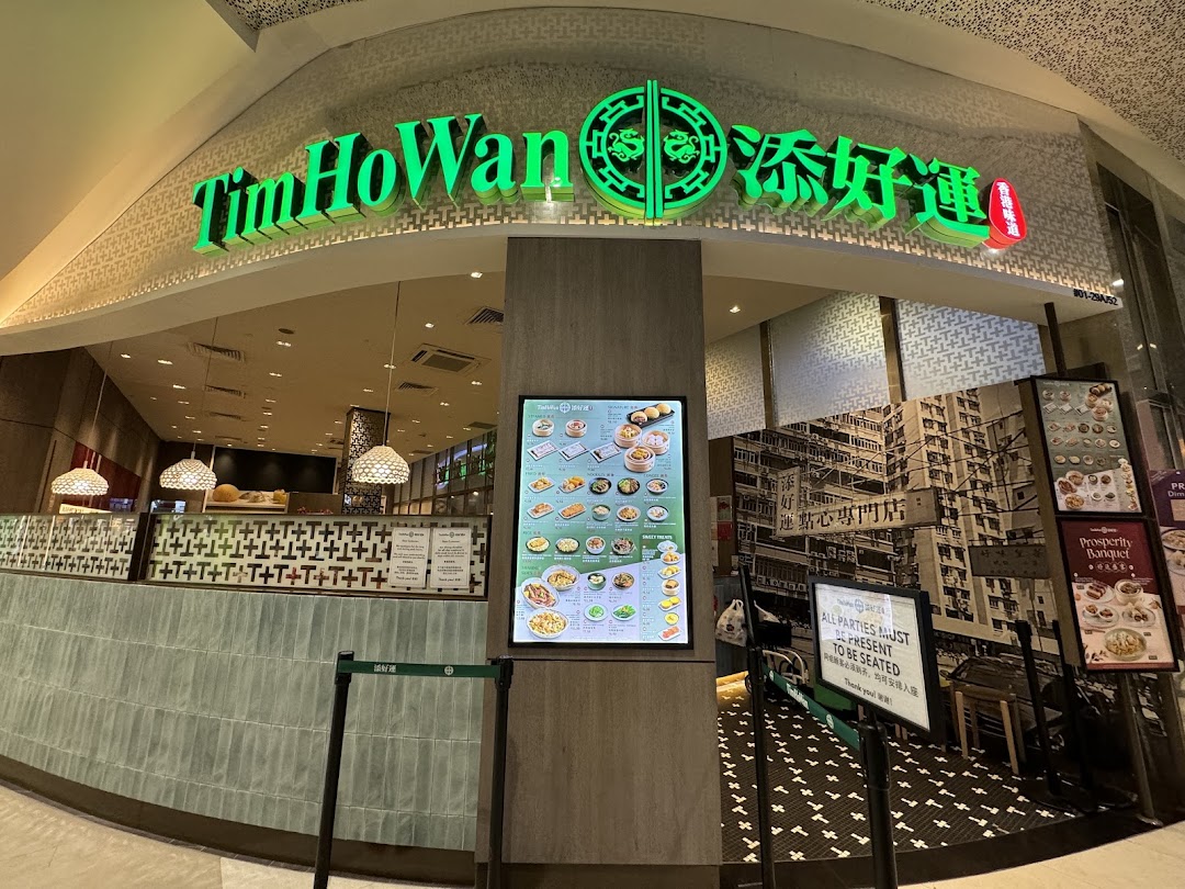 The exterior of Tim Ho Wan, a dim sum restaurant, featuring its vibrant green signage and a digital menu display.