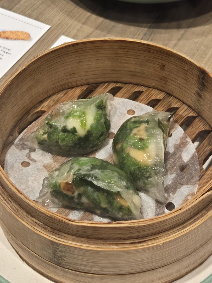 Three translucent steamed dumplings with green filling, likely vegetables, served in a traditional bamboo steamer.