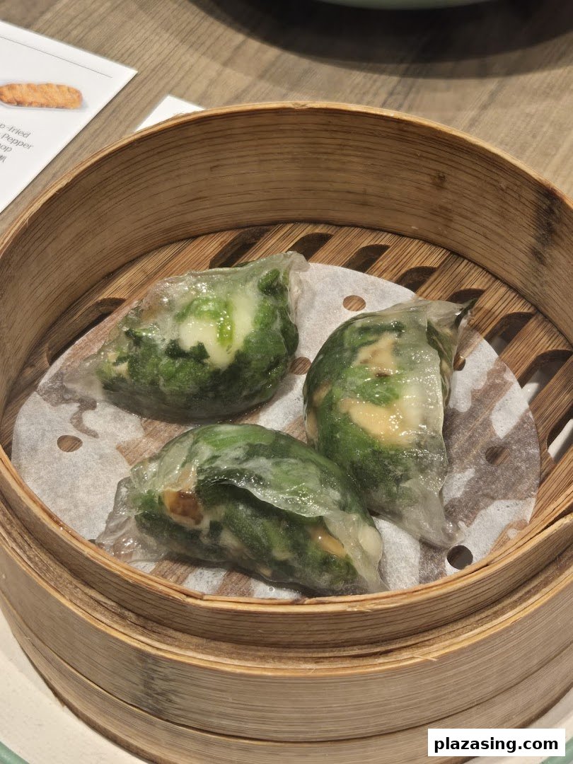Three translucent steamed dumplings with green filling, likely vegetables, served in a traditional bamboo steamer.