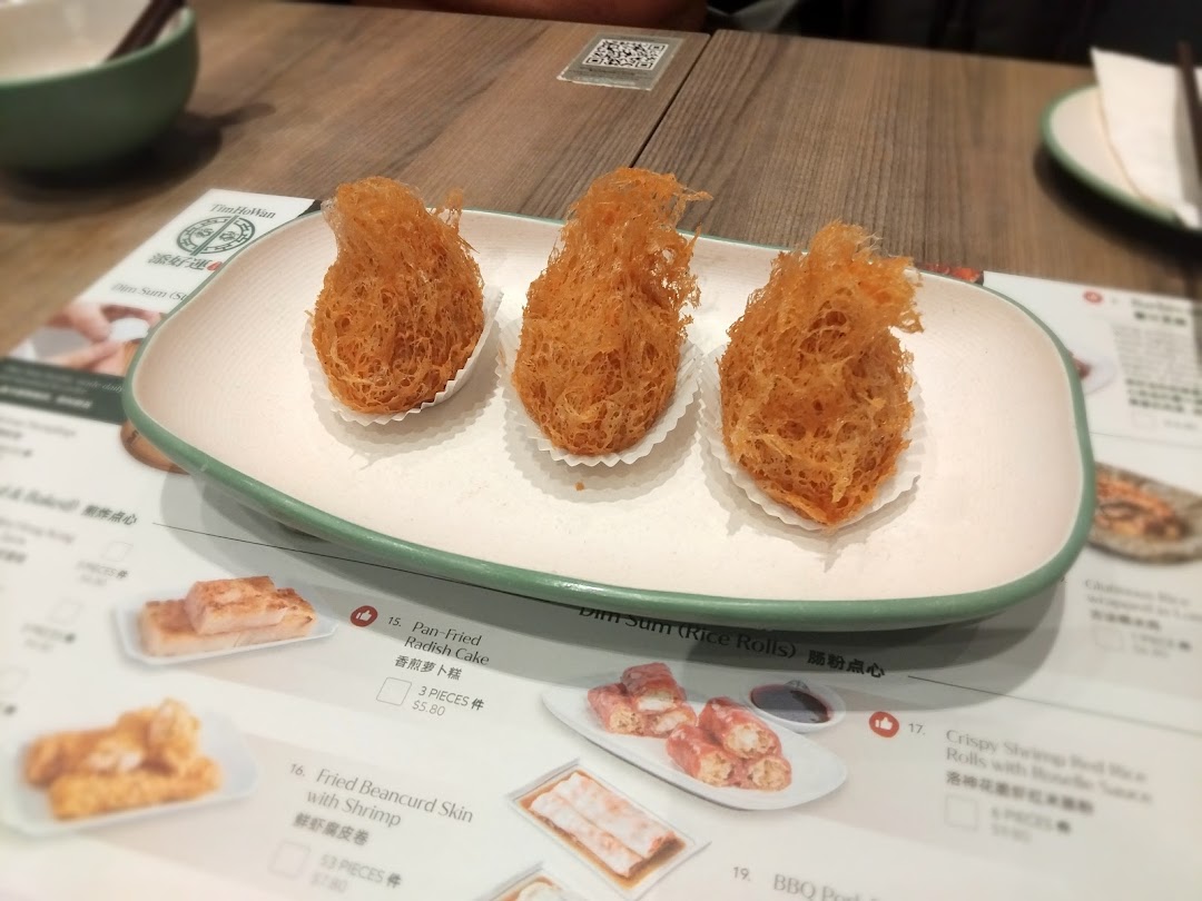 A plate of crispy fried dim sum on a table with a visible menu from Tim Ho Wan.