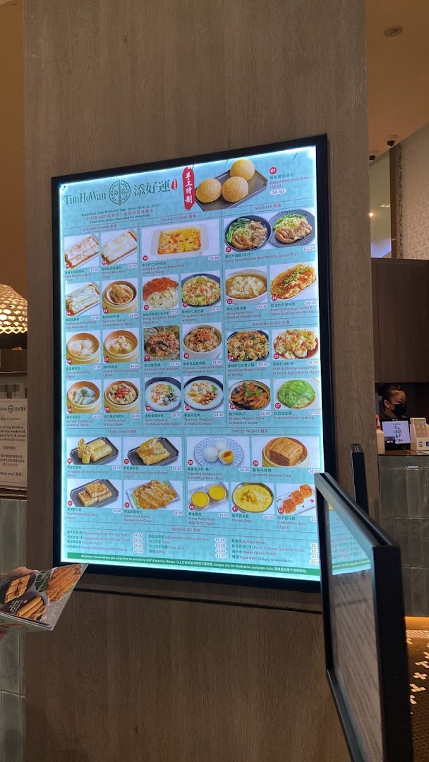 A brightly lit digital menu board at Tim Ho Wan showcasing various dim sum and Hong Kong-style dishes.