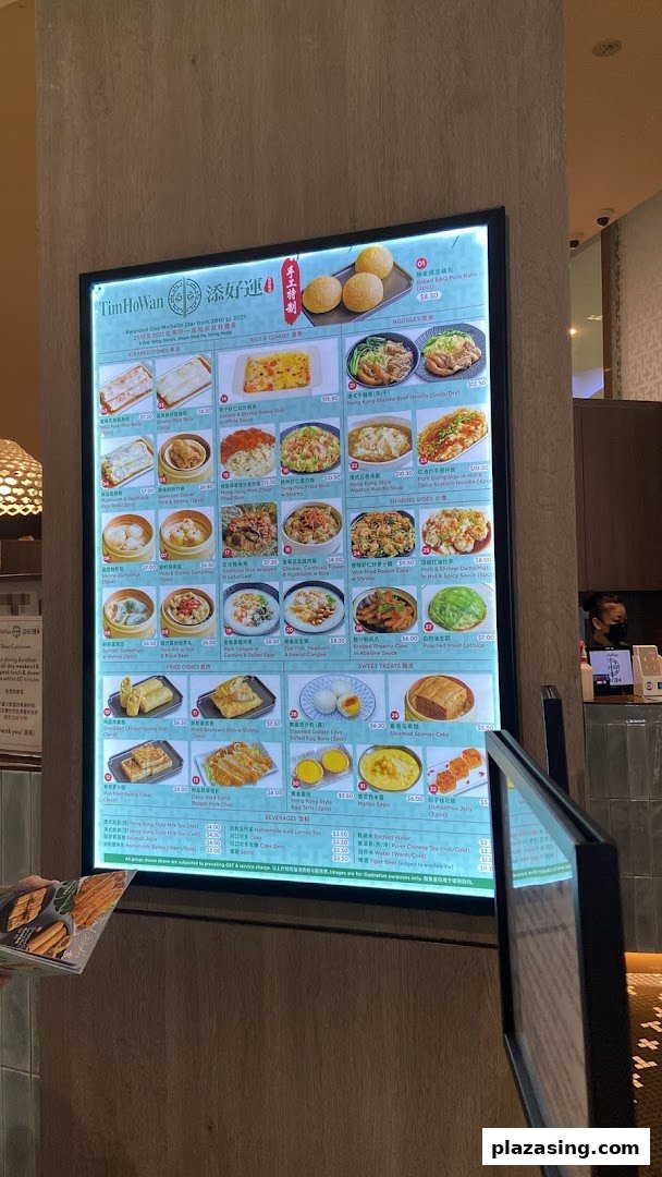 A brightly lit digital menu board at Tim Ho Wan showcasing various dim sum and Hong Kong-style dishes.