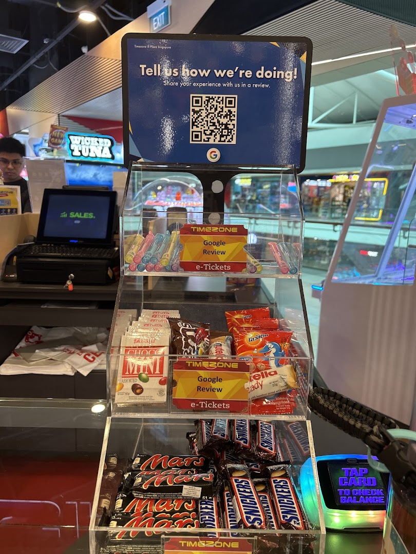 A Timezone counter featuring a customer feedback QR code, various snacks, and a game card balance checker.