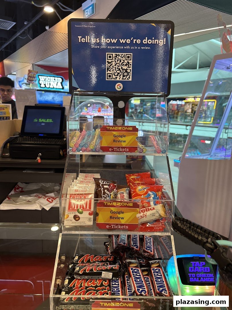 A Timezone counter featuring a customer feedback QR code, various snacks, and a game card balance checker.
