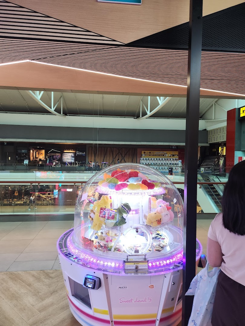 A brightly lit claw machine filled with plush toys inside a bustling shopping mall.