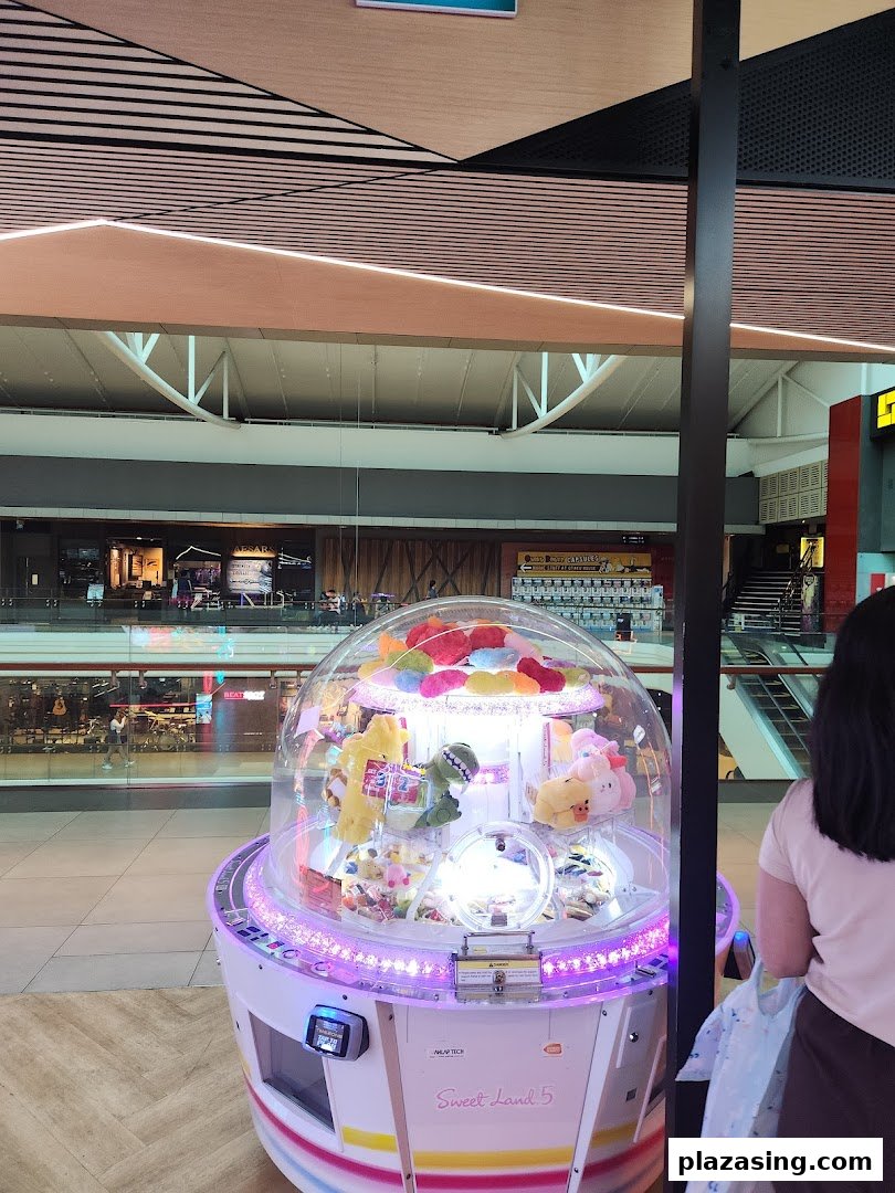 A brightly lit claw machine filled with plush toys inside a bustling shopping mall.