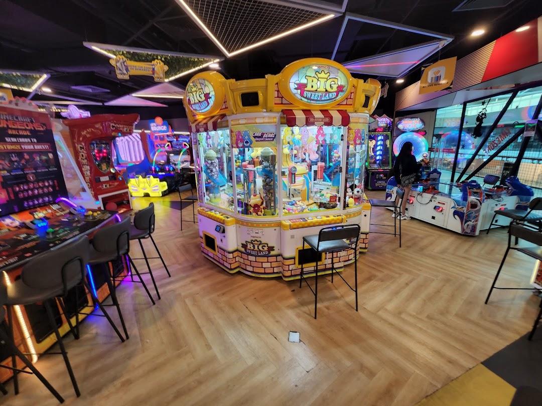 An arcade interior featuring various game machines, including a prominent 'Big Sweet Land' claw machine.