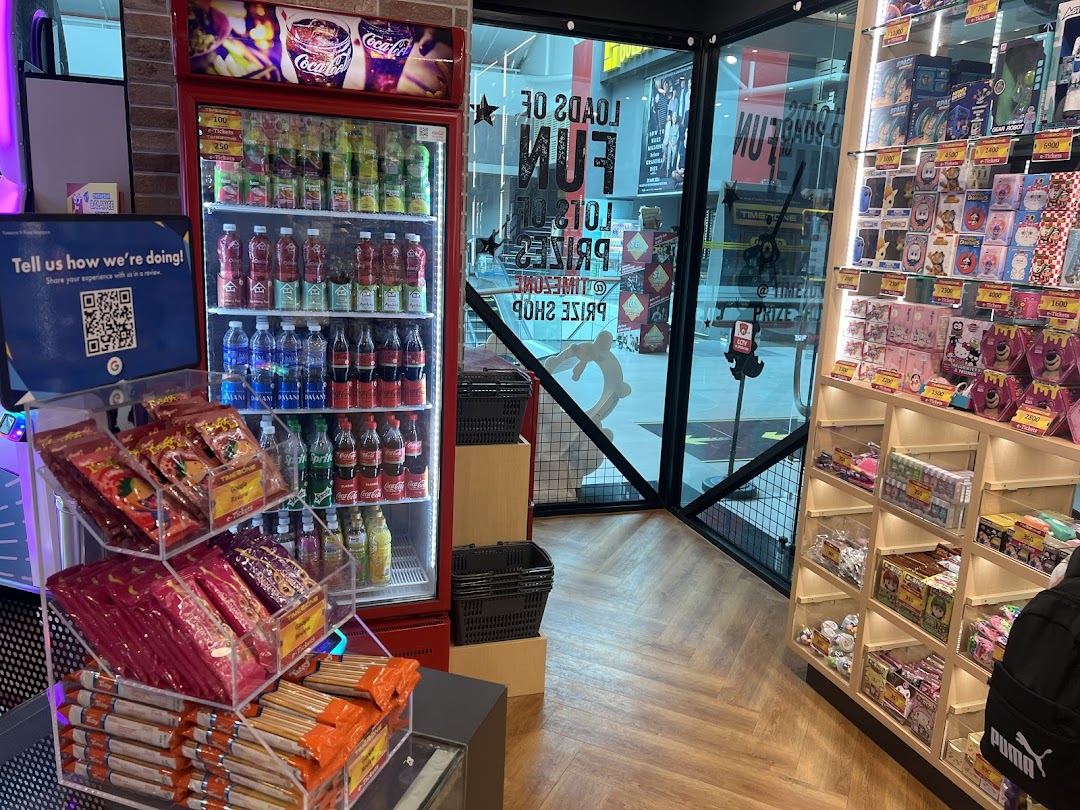 An arcade interior featuring a well-stocked drink fridge, a vibrant prize shop display, and a view of the entrance.