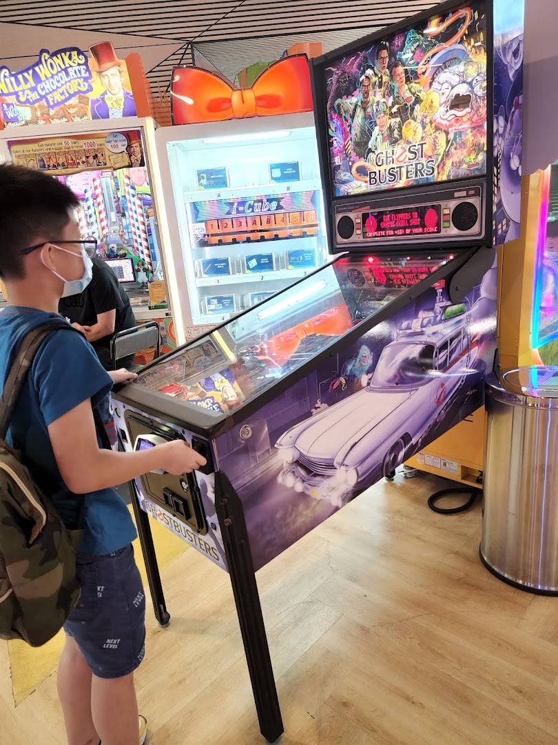 A person plays a Ghostbusters pinball machine inside Timezone arcade, surrounded by other games.