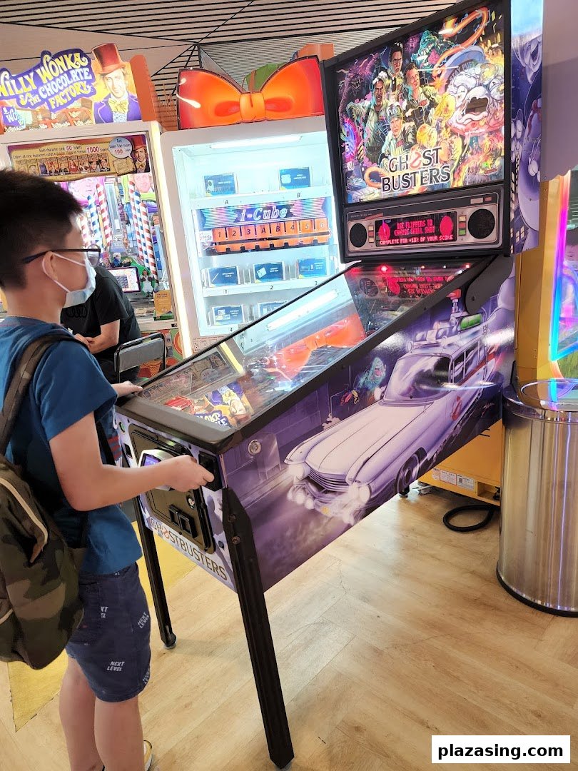 A person plays a Ghostbusters pinball machine inside Timezone arcade, surrounded by other games.