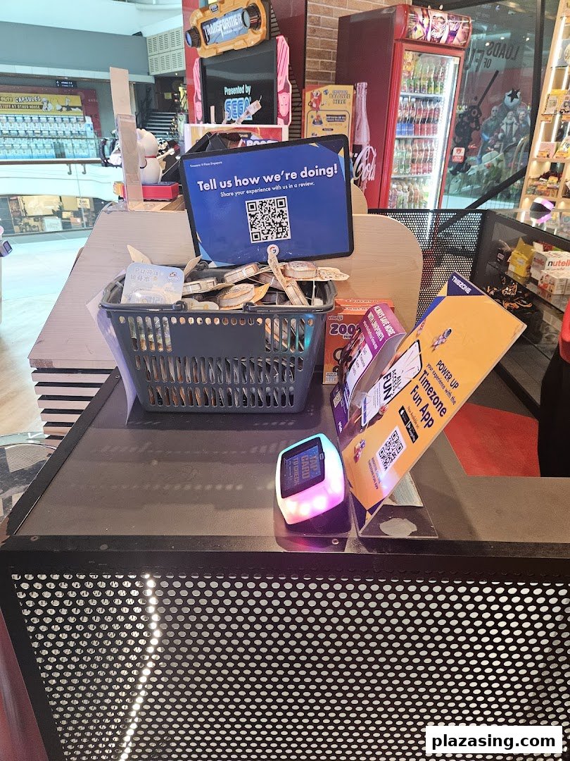 A counter at Timezone arcade with a customer feedback sign, prize basket, and arcade games in the background.