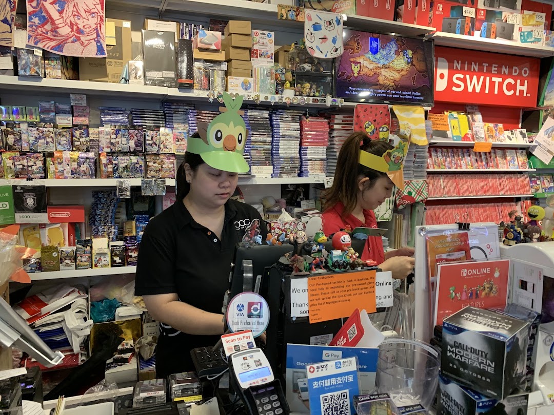 Two staff members at the counter of TOG - Toy Or Game Plaza Singapura, surrounded by games and collectibles.