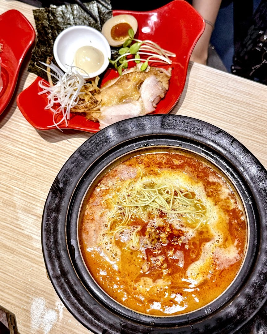 A vibrant hotpot with noodles and a side dish of chicken, egg, and vegetables.