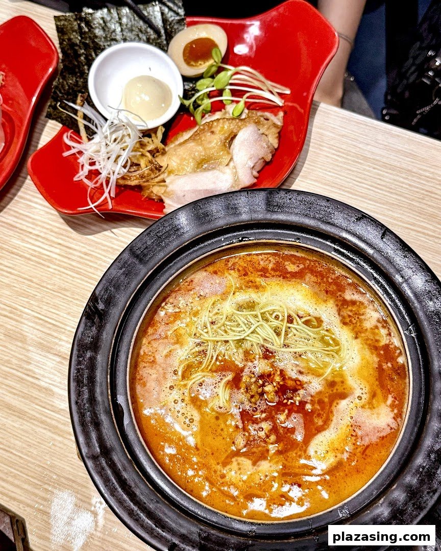 A vibrant hotpot with noodles and a side dish of chicken, egg, and vegetables.