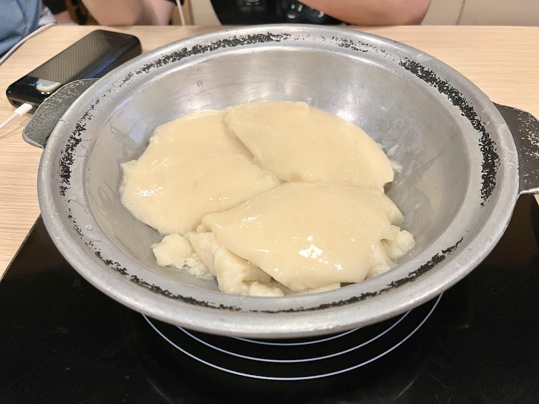 A metal pot filled with creamy, collagen-rich chicken stock on an induction cooker.